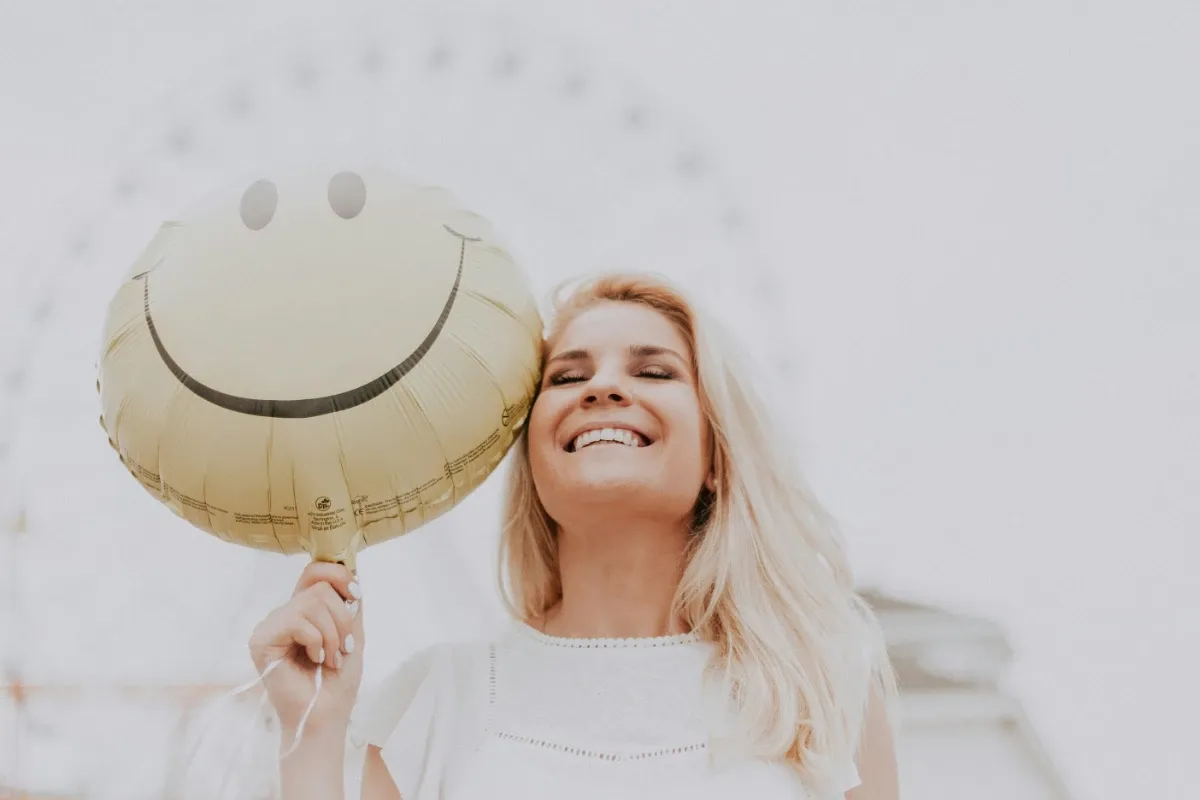 A healthy woman smiling holding a smiley baloon.