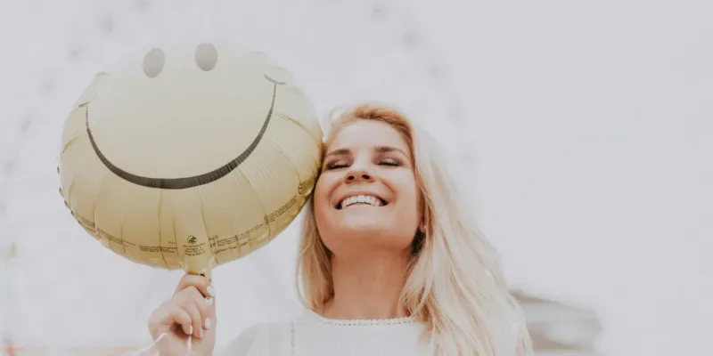 A healthy woman smiling holding a smiley baloon.